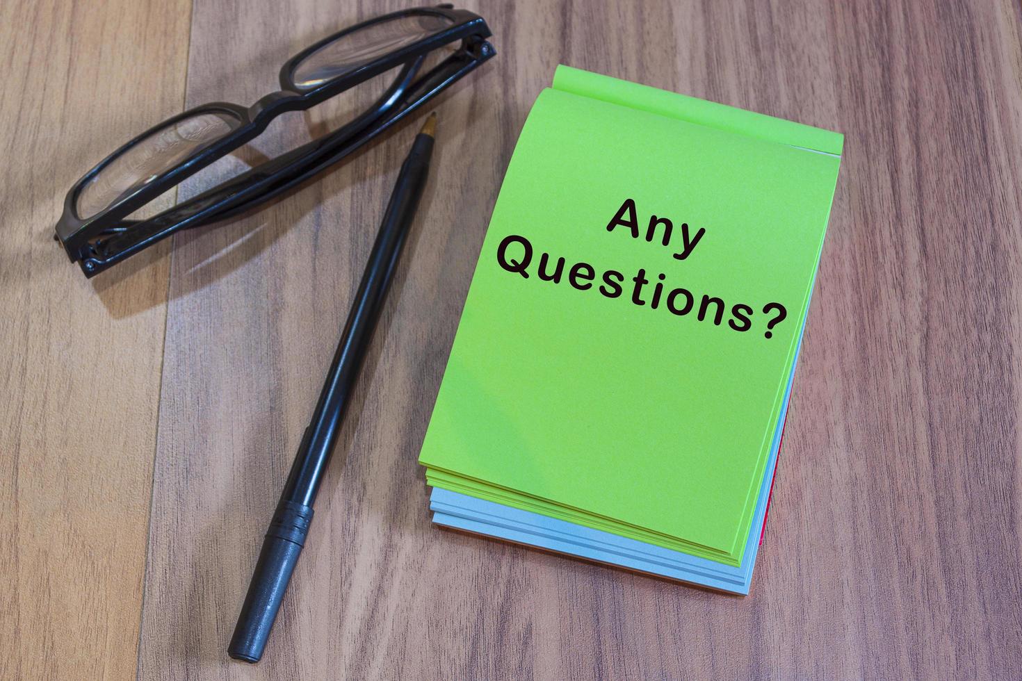 Any question with punctuation mark text on green notepad with glasses and pen on a desk photo