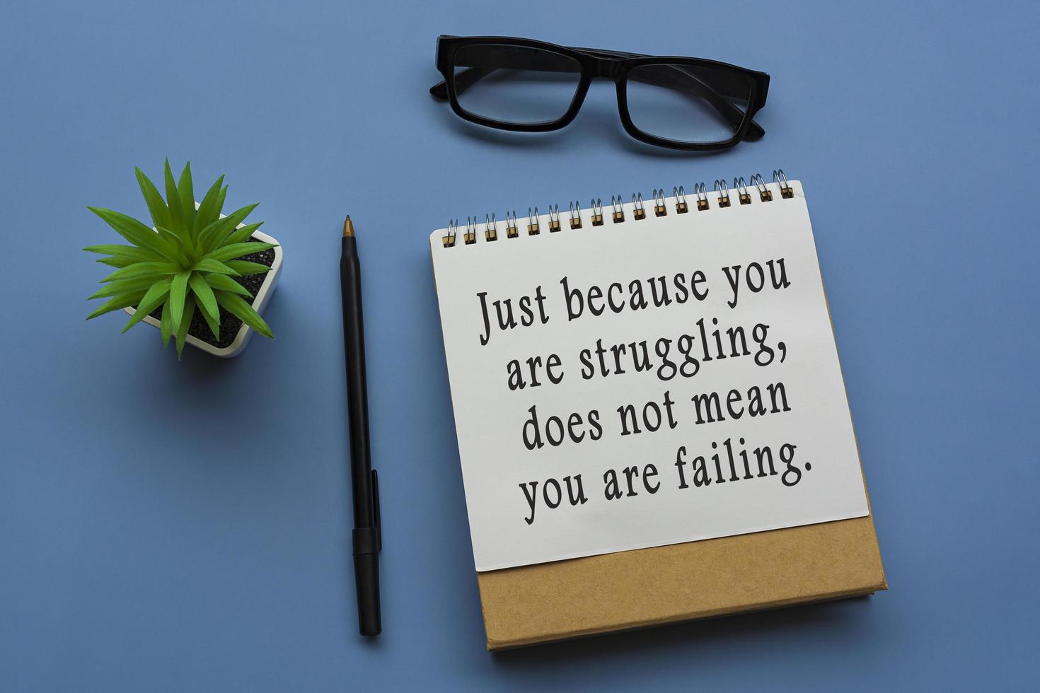 Motivational quote on notepad with potted plant, glasses and a pen photo