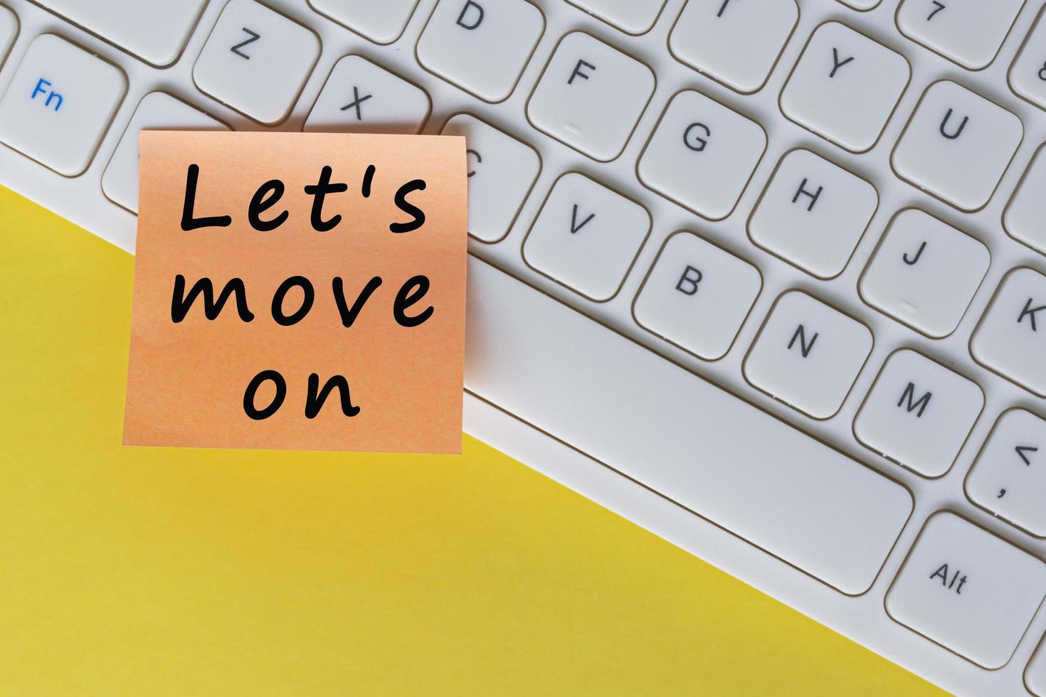 Let's move on text on orange sticky note on top of white keyboard. photo