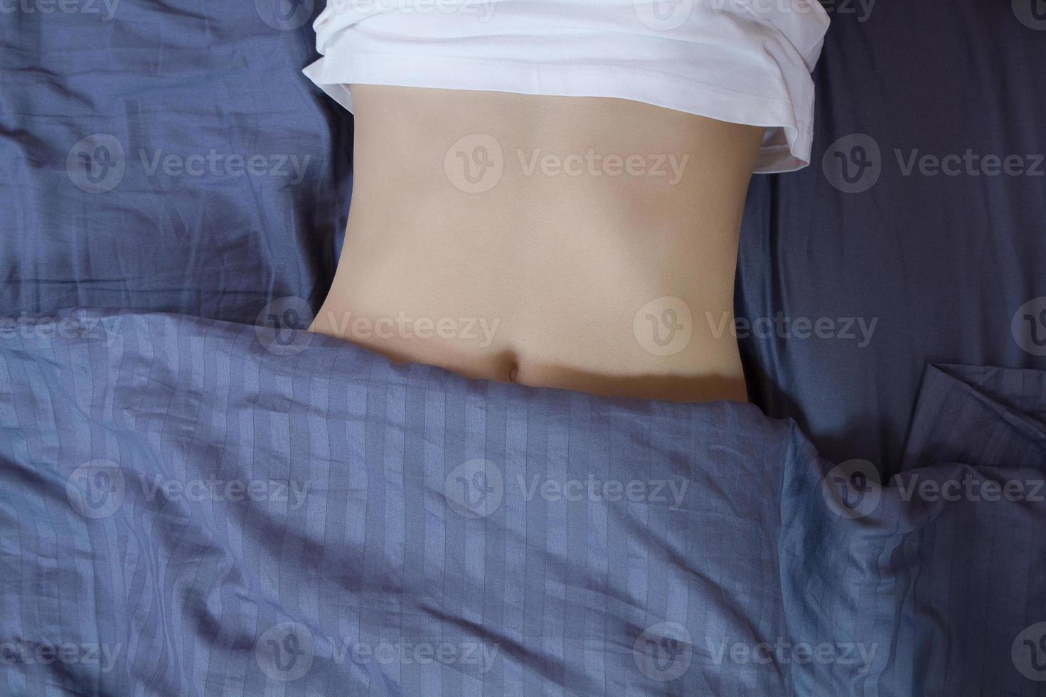 Healthy nutrition and belly health concept. Close up of woman flat stomach. Girl in bed with hungry feeling. Top view photo