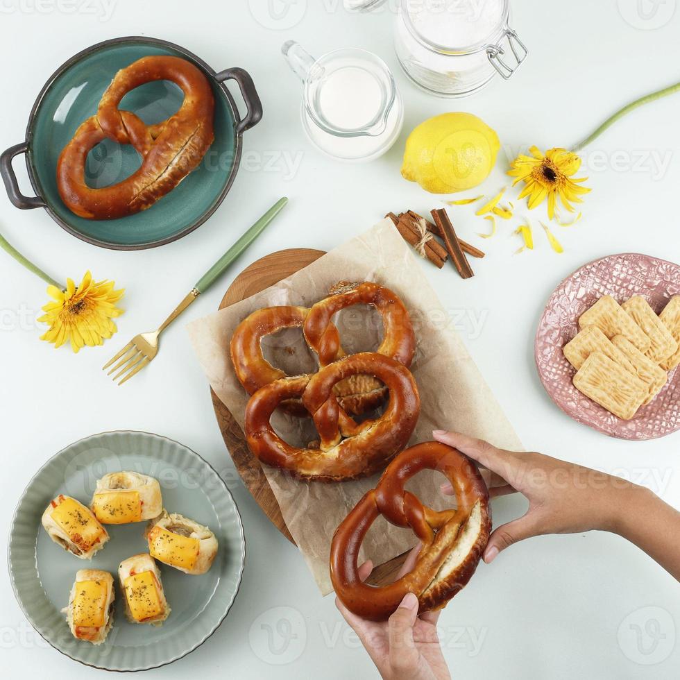 vista superior tiempo de merienda plano con mano, pretzel, galleta y rollo de hojaldre con queso derretido. adecuado para feeds de redes sociales o publicidad foto