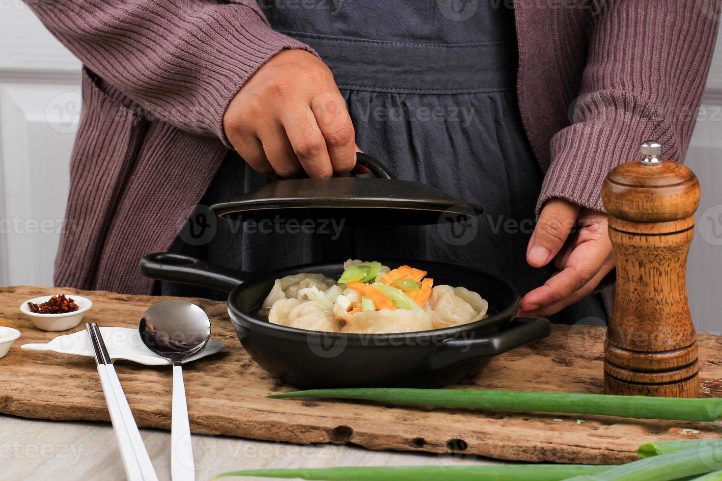 Asian Female Home Chef Cooking Dim Sum Soup Mandu Guk, Korean Dumpling Soup with Spring Onion Topping and Sliced Fried Egg above the Stove. Put Sliced Spring Onion photo