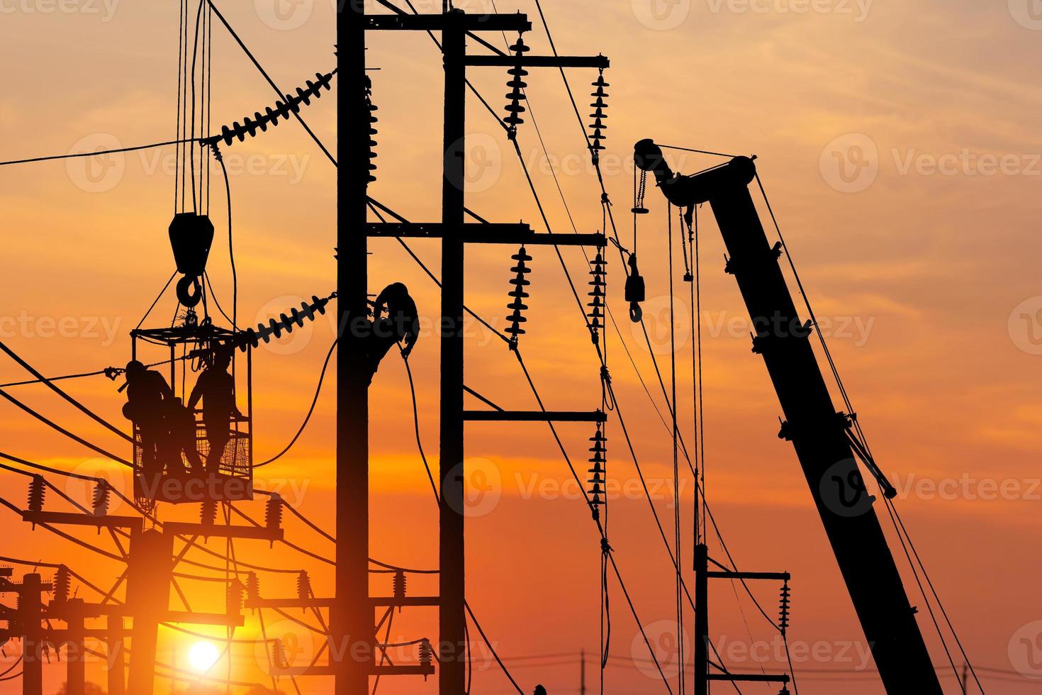 Silhouetted electrician team working on poles to install high-voltage equipment, Silhouette electrician on electric power pole with blurred sunset sky background photo