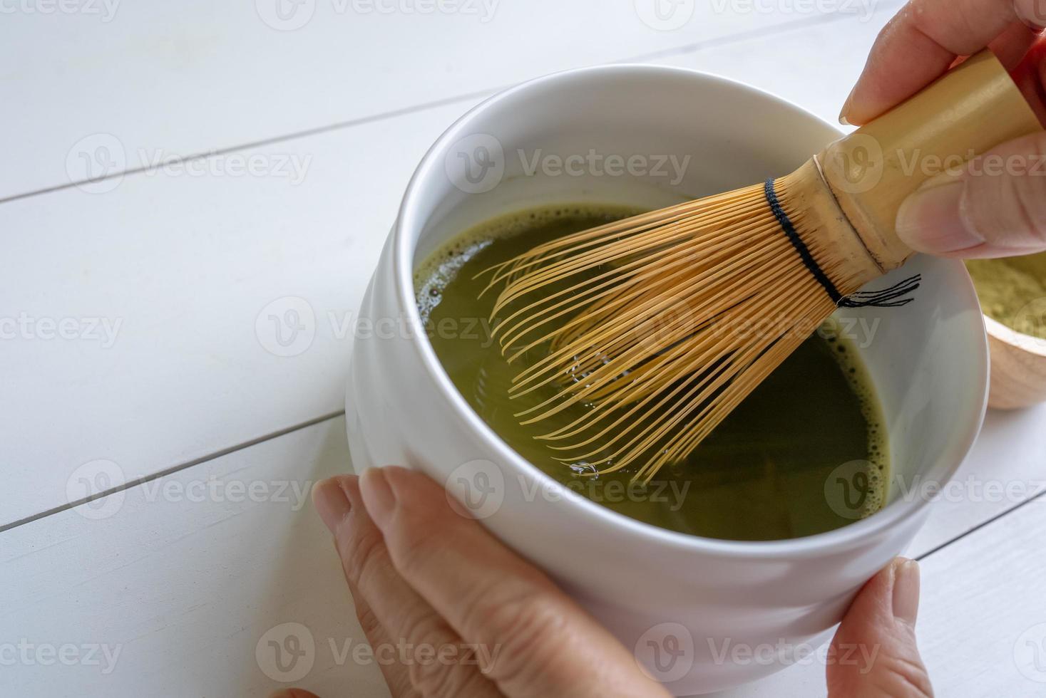 Woman Using Bamboo Whisk to Mix Matcha Green Tea Powder With Water photo