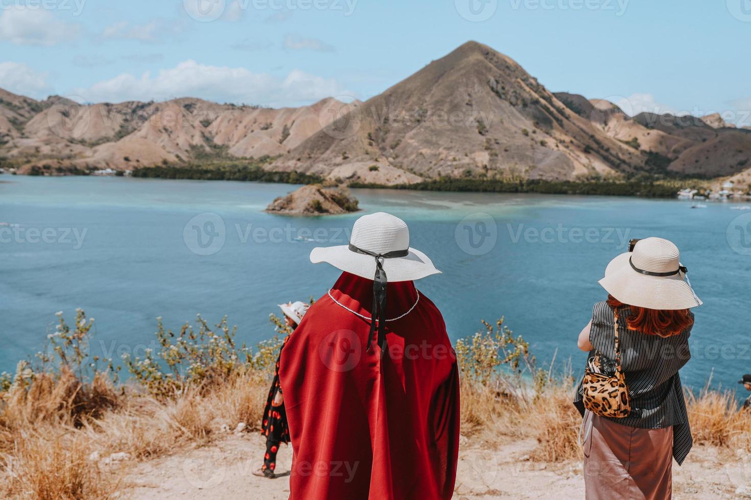 mujeres turistas con sombrero de verano de pie mientras miran hermosos paisajes marinos y colinas en labuan bajo foto