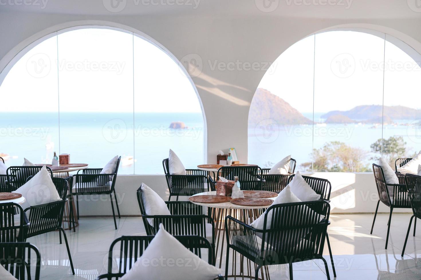 mesas y sillas negras con almohada en el comedor con vista al mar desde la ventana foto