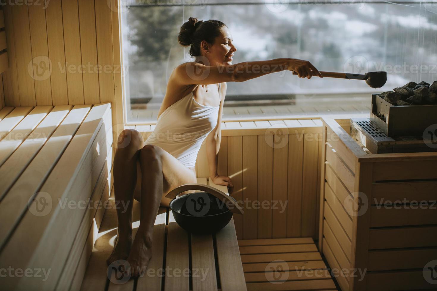 mujer joven vertiendo agua en piedra caliente en la sauna foto