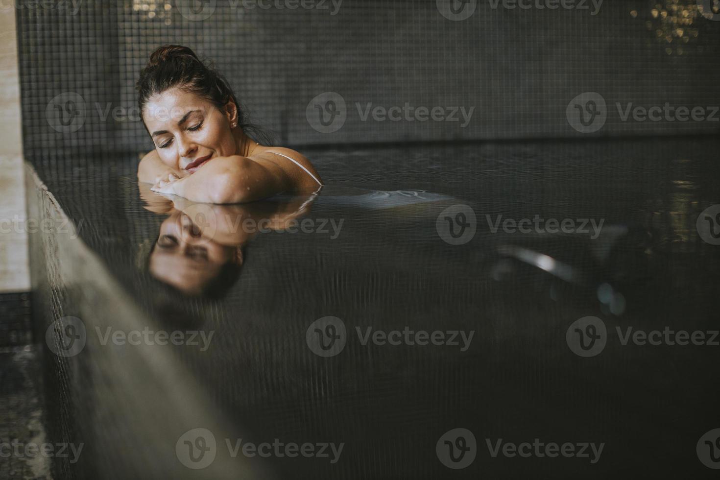 Young woman relaxing on the poolside of indoor swimming pool photo