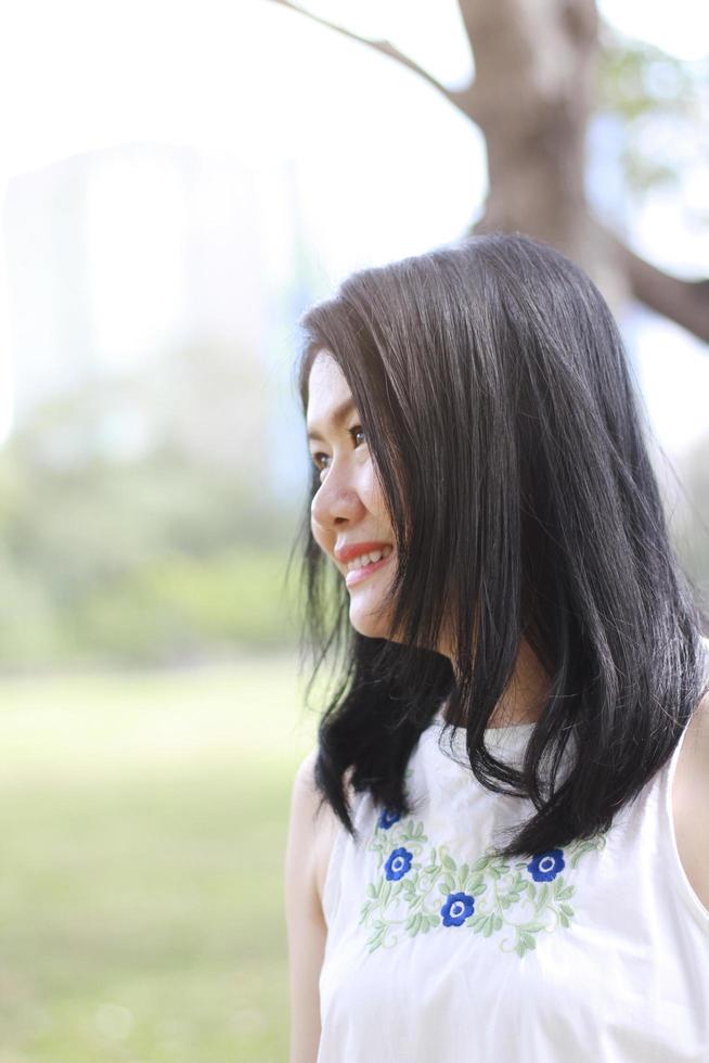 bella mujer asiática vestida de blanco relajada y sonriente en el parque natural. niña tailandesa o niña china disfrutan de vacaciones con la luz del sol en el jardín foto