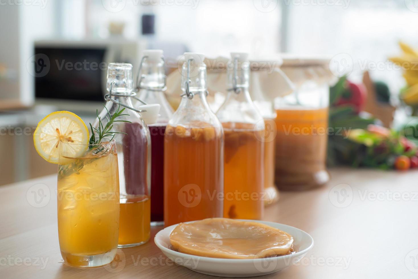Kombu tea in a glass with ice, lemon slices and rosemary leaves, Homemade fermented raw kombucha tea in bottles and glass jars mix with fruit juice and scoby on table.Healthy natural probiotic drink. photo