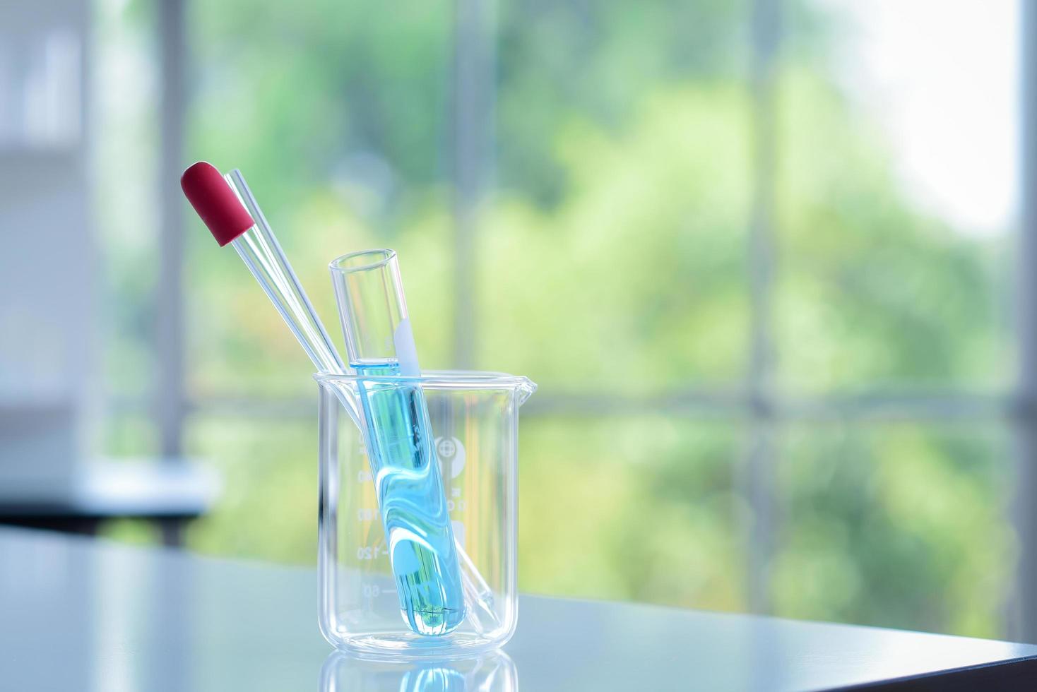 el tubo de ensayo con el interior químico azul se colocó con un cuentagotas y una varilla de vidrio dentro del vaso de precipitados sobre la mesa en el laboratorio químico para preparar el experimento foto