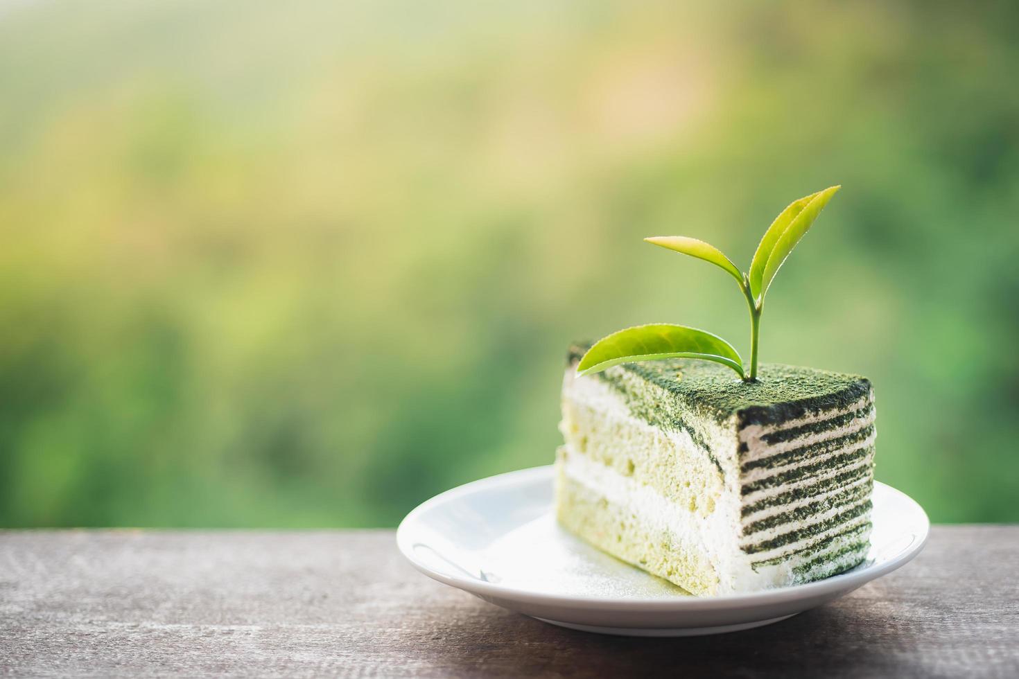 hoja de té de primer plano sobre bizcocho de dos capas de té verde matcha y crema con polvo de té verde matcha espolvoreado encima en un plato blanco colocado sobre una mesa de madera. foto