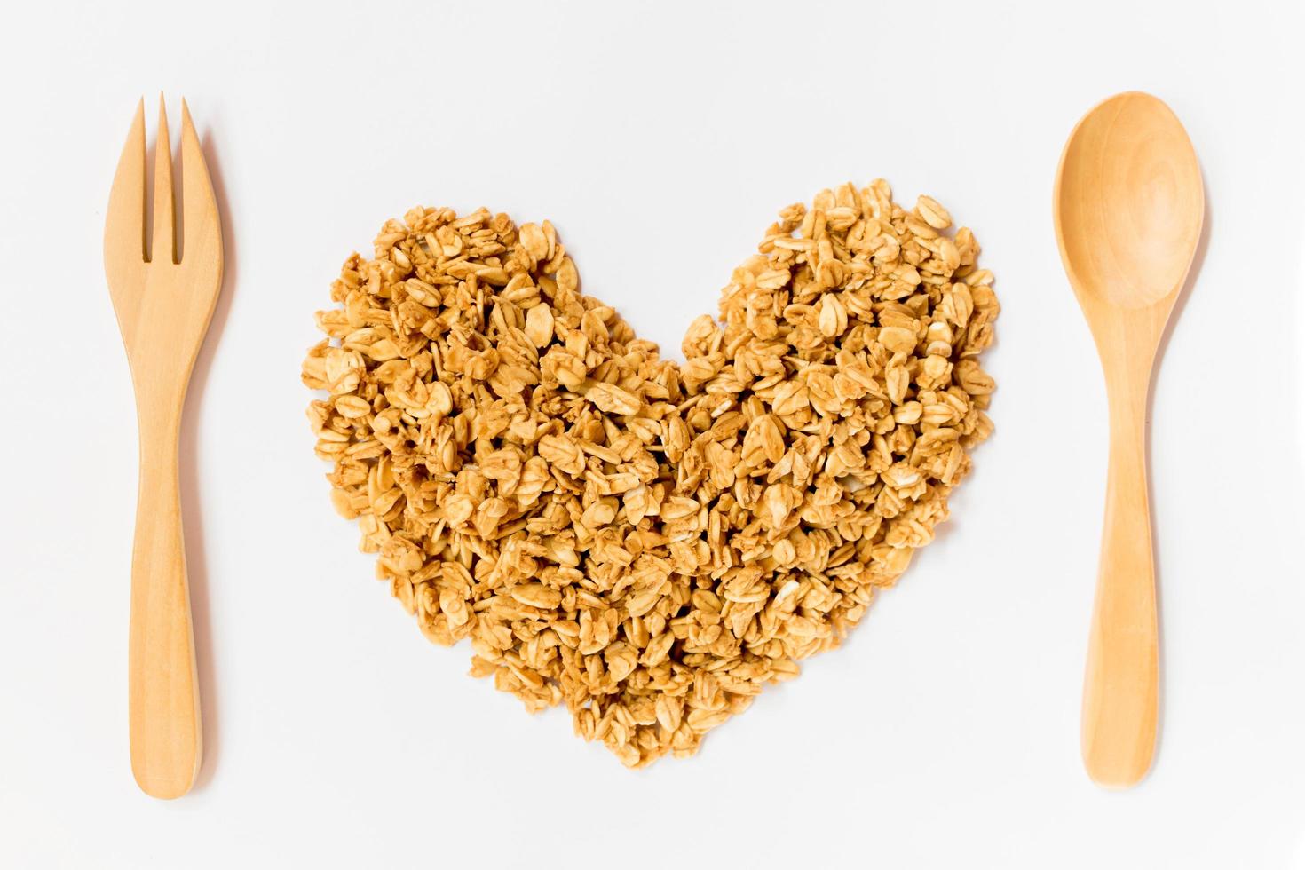 primer plano de copos de avena sin cocer en forma de corazón con cuchara y tenedor de madera aislado sobre fondo blanco. comida, comida cruda, día de san valentín. foto