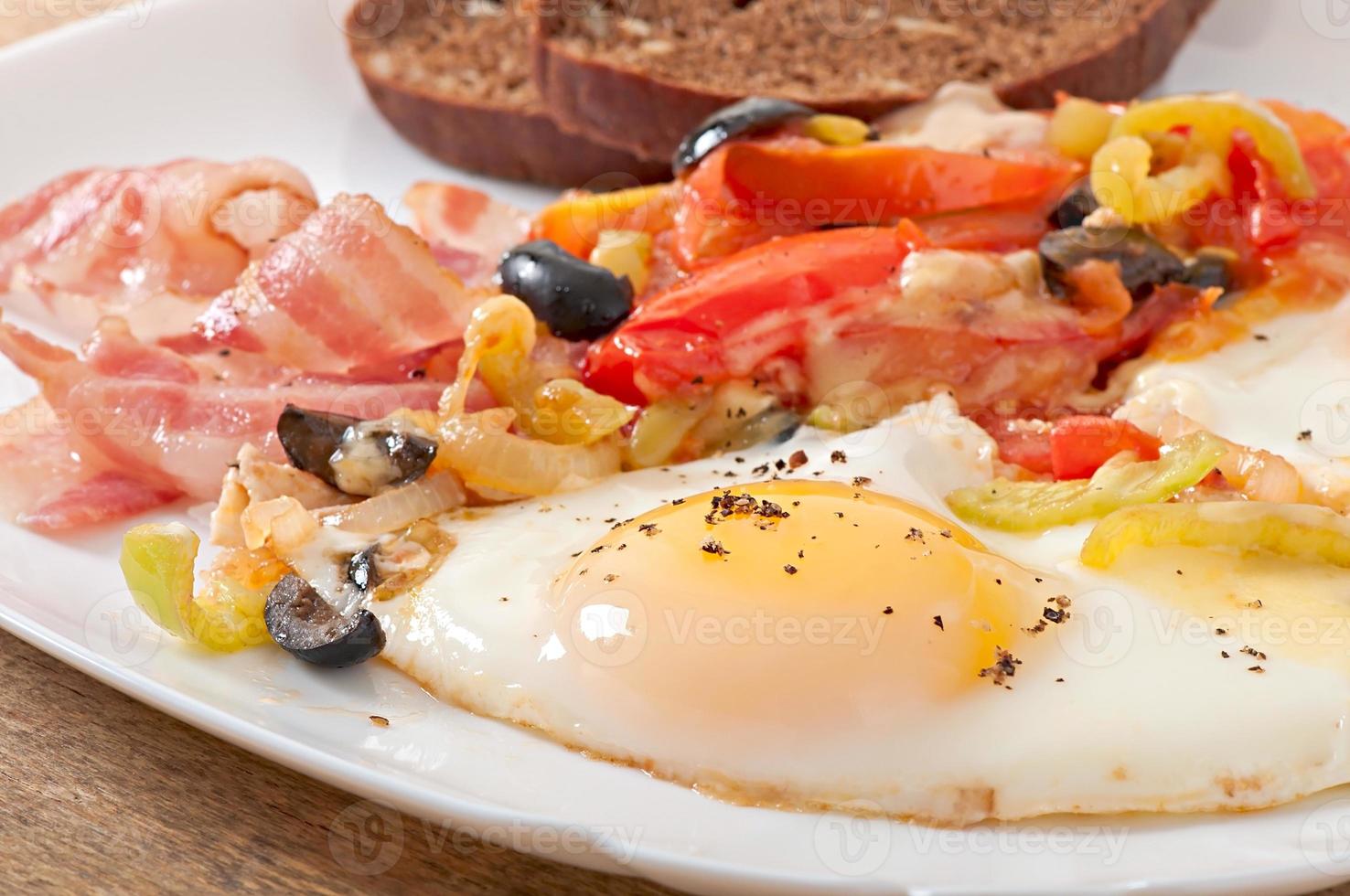 Breakfast - fried eggs with bacon, tomatoes, olives and slices of cheese photo