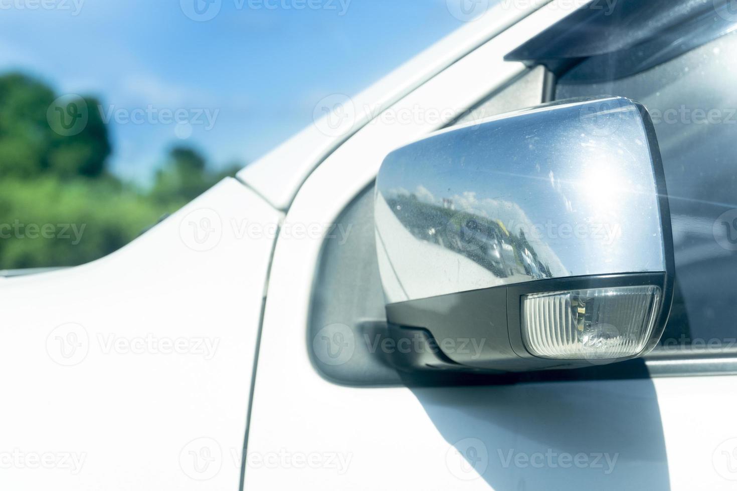 Close up side mirror wing of car  is foldable parking time. parking outdoor at day time. with blurred of trees under blue sky. photo
