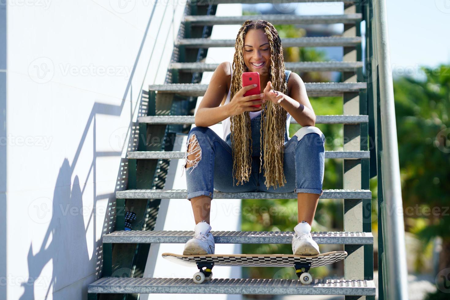 Una alegre patinadora negra navegando por un smartphone en la ciudad foto