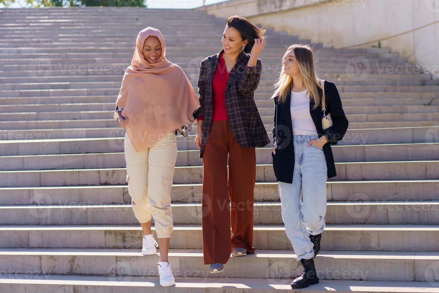 Positive young diverse women friends walking downstairs in campus photo