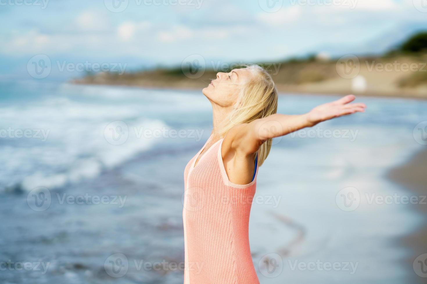 Beautiful mature woman opening her arms on a beautiful beach, enjoying her free time photo
