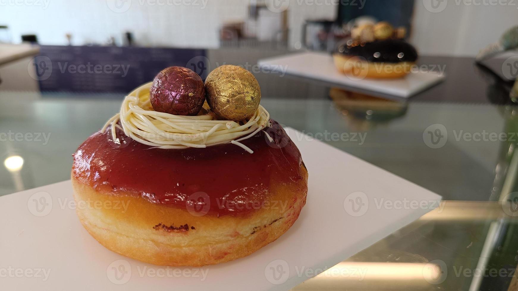 Donut glazed strawberry and decorated with red and gold easter eggs on white plate photo