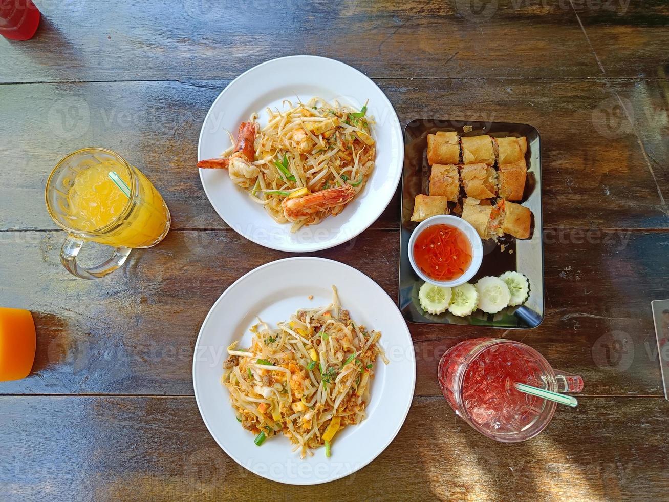 pad thai en la mesa servido con jugo de naranja, jugo de roselle y rollitos de primavera fritos. comida tailandesa popular, vista superior foto