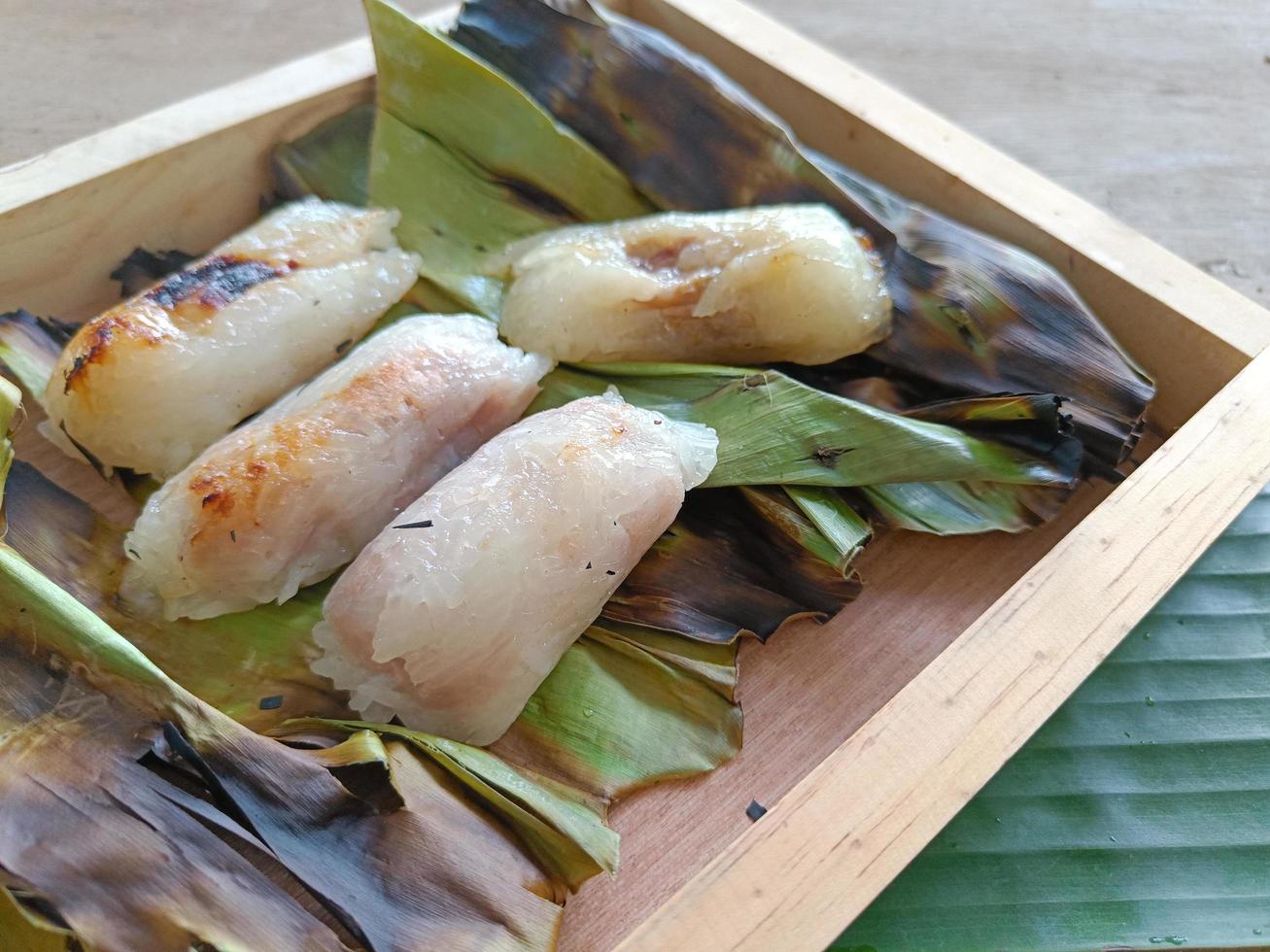 arroz glutinoso relleno a la parrilla envuelto en hojas de plátano o arroz pegajoso con plátano y taro en un plato de madera. antiguo menú de estilo tailandés de arroz pegajoso. el nombre tailandés es khao niao ping foto