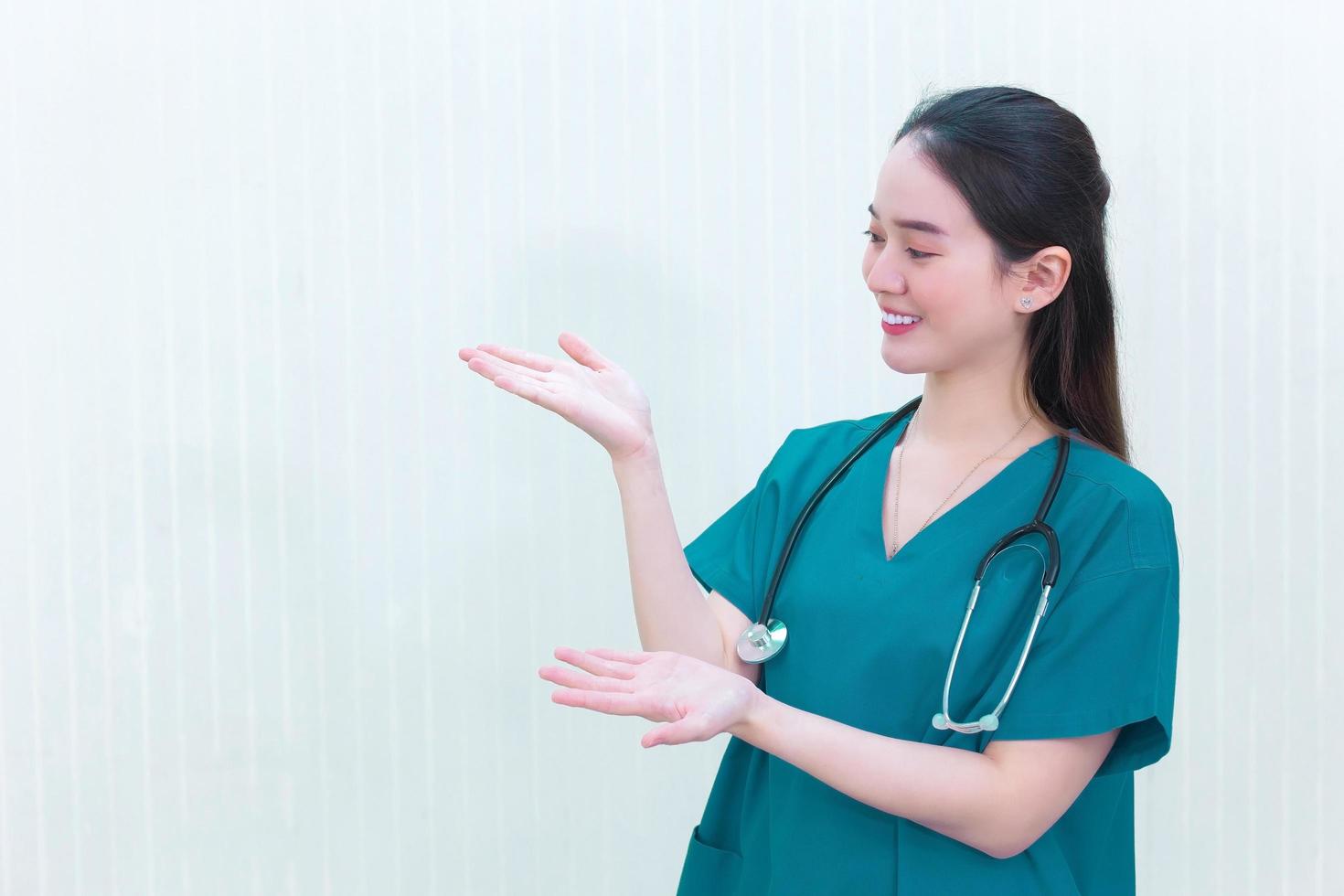 una doctora profesional asiática con un uniforme verde se pone de pie y sonríe mientras señala la parte superior sobre un fondo blanco. foto