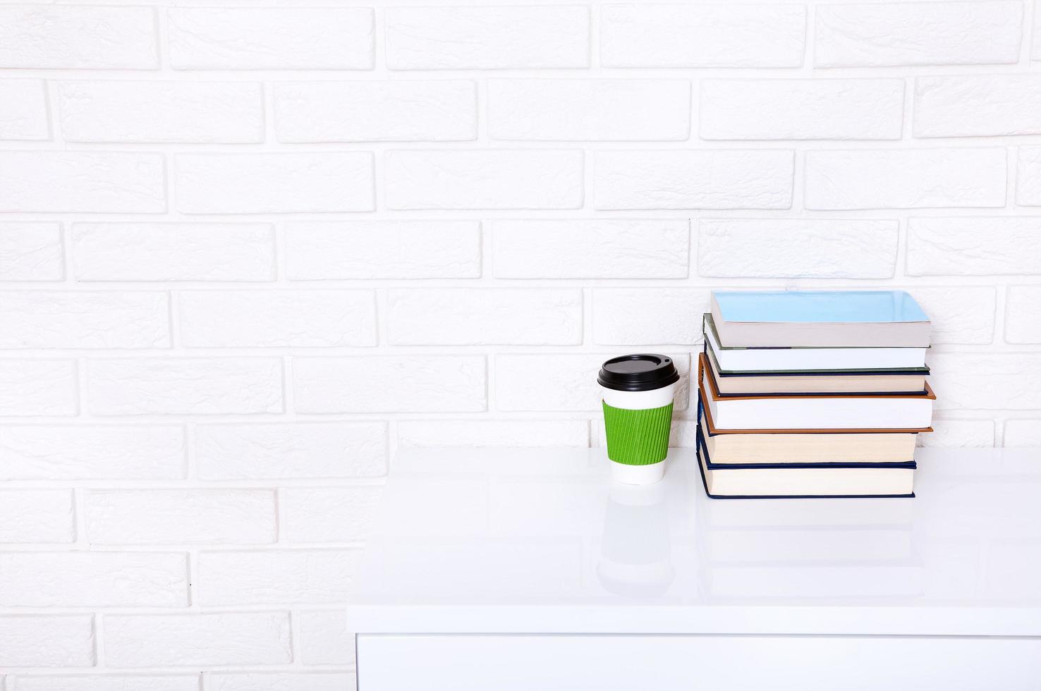 Many books and a cup of coffee on white table near brick wall in the office. Copy space and selective focus photo