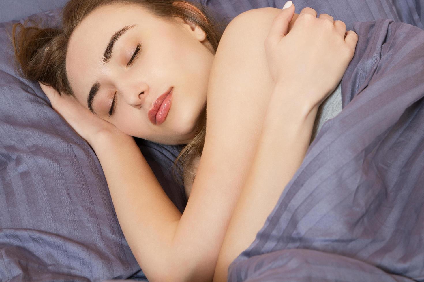 Sleep. Woman sleeping in bed having beauty sleep in pajamas. Beautiful cute girl in her twenties. Asian Caucasian female model in full body lying down. photo