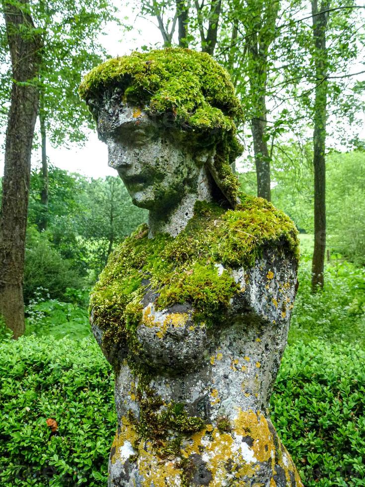 ertical shot of an old statue covered in moss in a forest photo