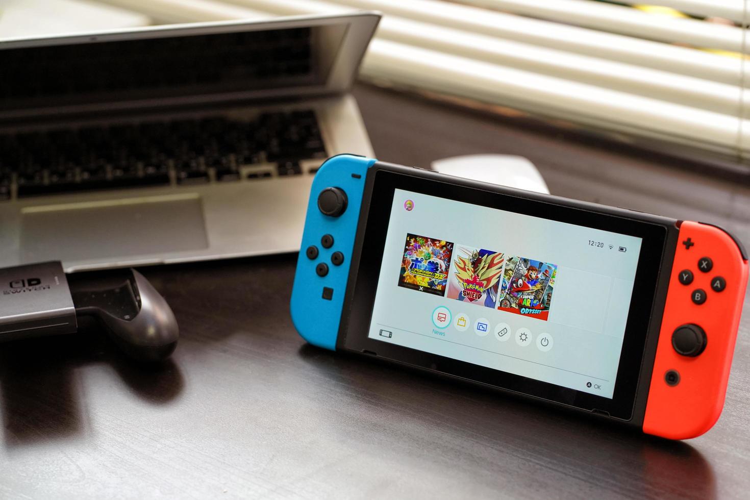 bangkok tailandia-10 de abril de 2022 consola de videojuegos nintendo switch y controlador joy-con para juegos domésticos o portátiles en la oficina de escritorio con fondo de computadora portátil. foto