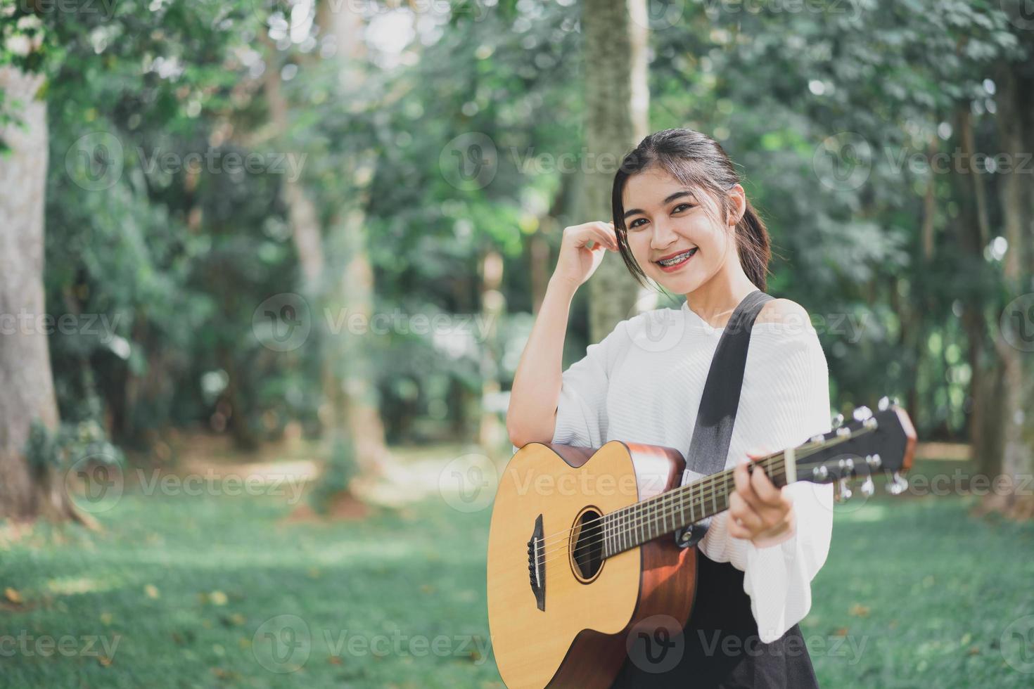 joven asiática tocando guitarra y cantando música en el parque, mujer asiática tocando guitarra en el jardín foto