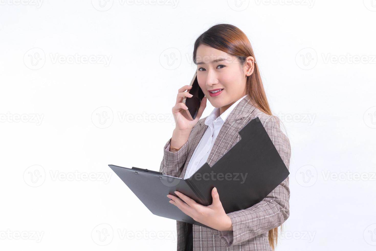 Asian working woman in formal suit with white shirt is calling telephone and opens document file or clipboard to check data. photo