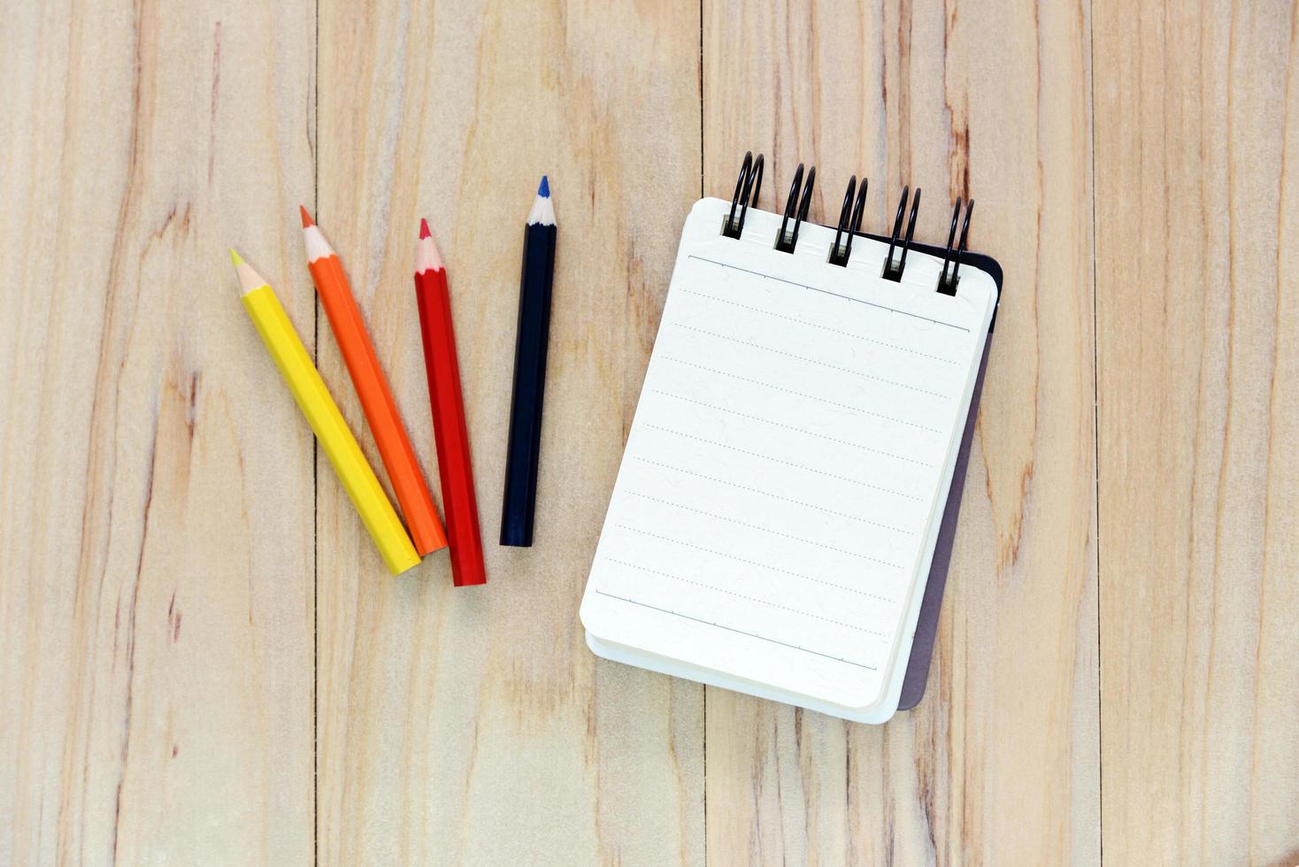 Small note book paper or notepad for writing information with color pencil  on wooden table. view from above photo