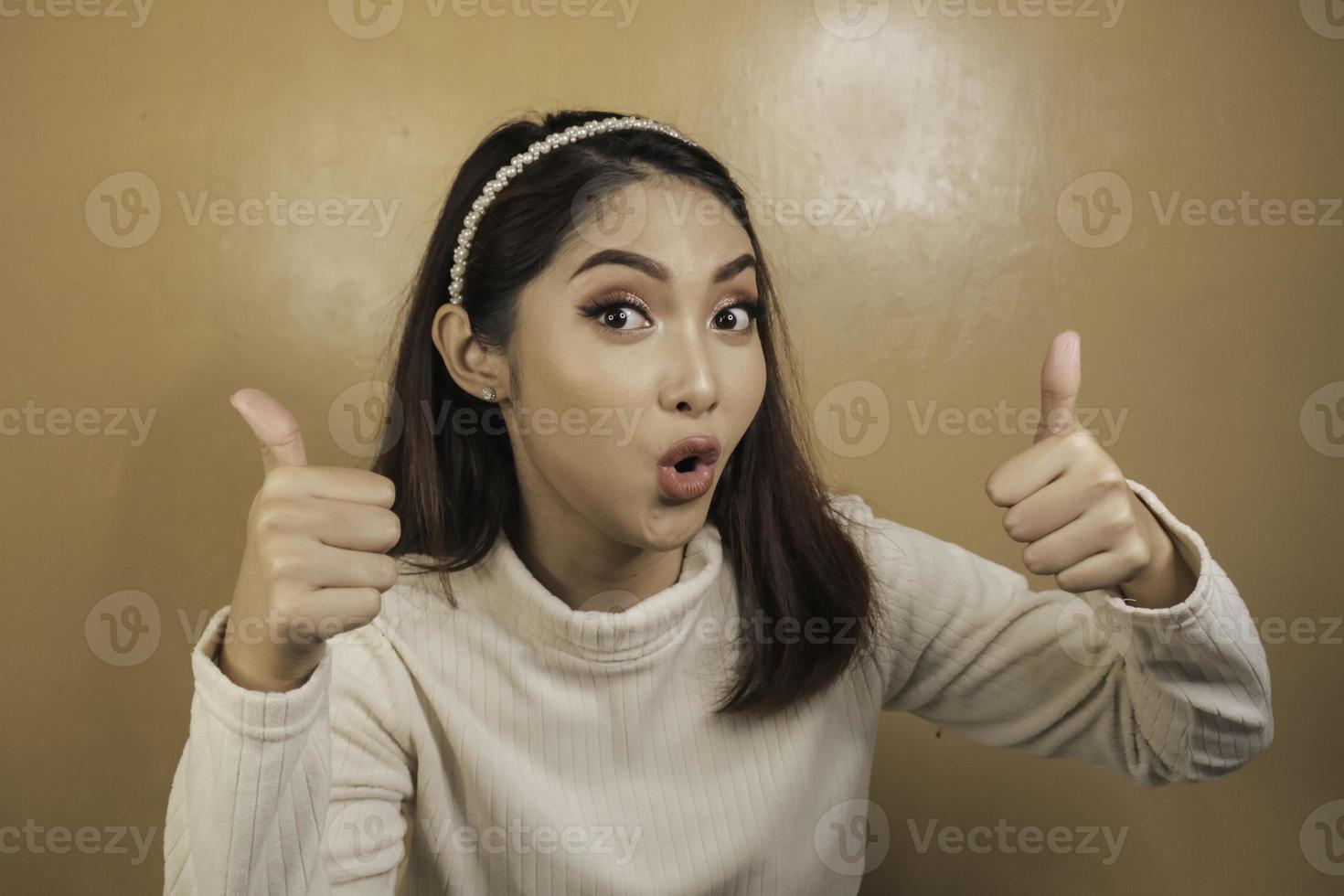 Shock face of a young Asian woman with OK sign wearing a white shirt. Advertisement concept. photo