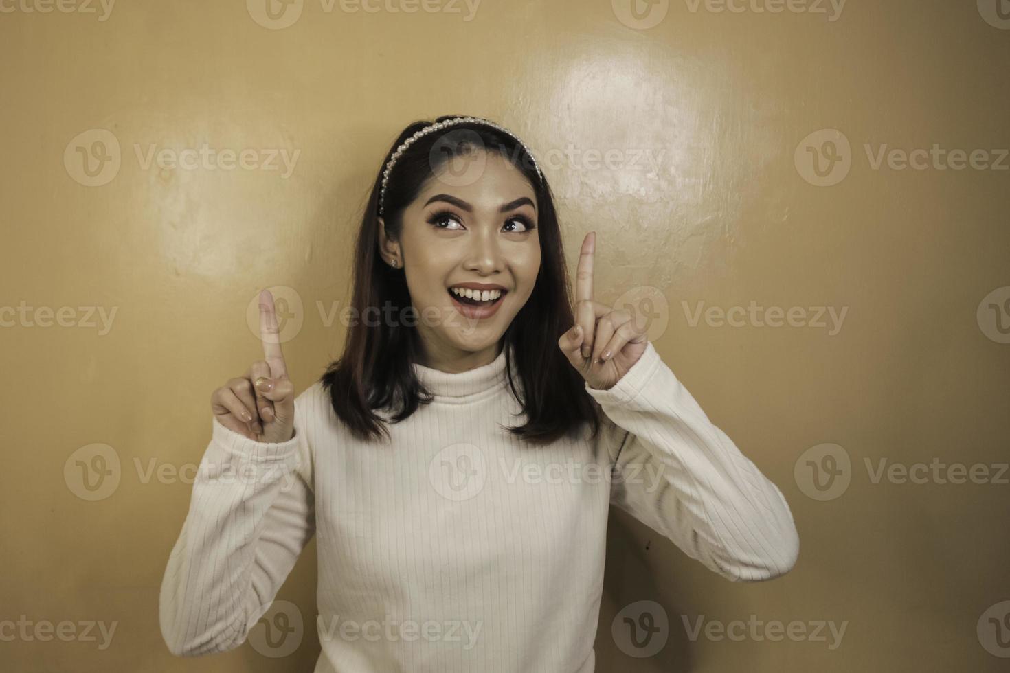 Happy young asian woman with hand point above on empty space photo