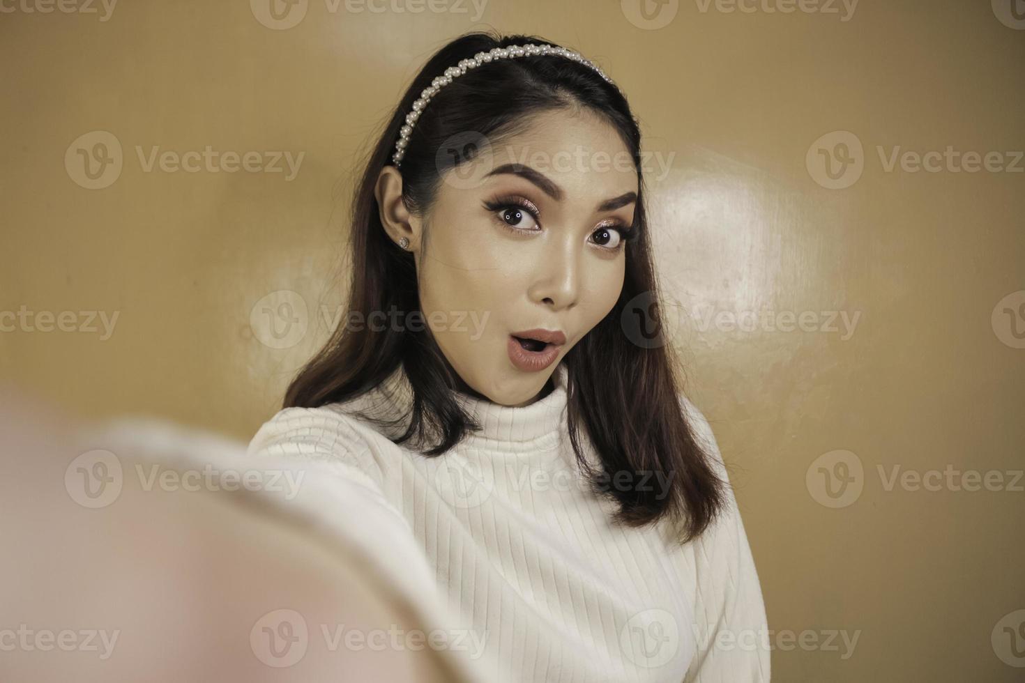 Young Asian woman is smiling and selfie taking pictures with her mobile phone. Indonesian woman on orange background. photo