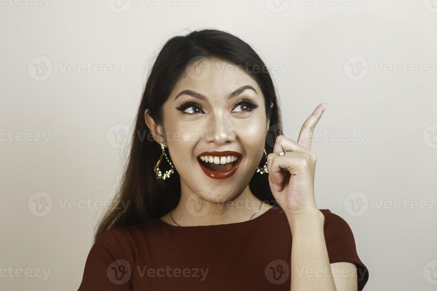 Shock face of a young Asian woman wearing a red shirt pointing upwards. Advertisement concept. photo