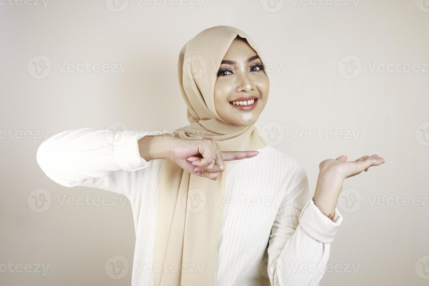 Cheerful young Muslim Asian woman pointing side to copy space with smile photo