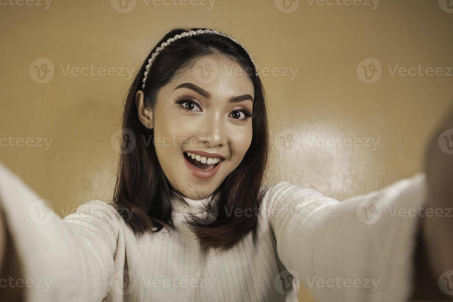Young Asian woman is smiling and selfie taking pictures with her mobile phone. Indonesian woman on orange background. photo