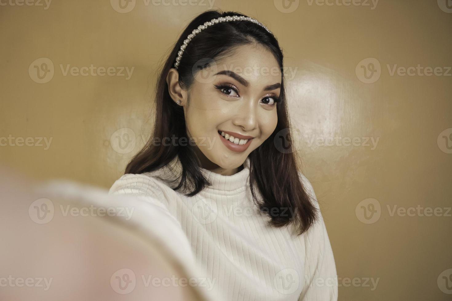 joven asiática está sonriendo y selfie tomando fotos con su teléfono móvil. mujer indonesia sobre fondo naranja.