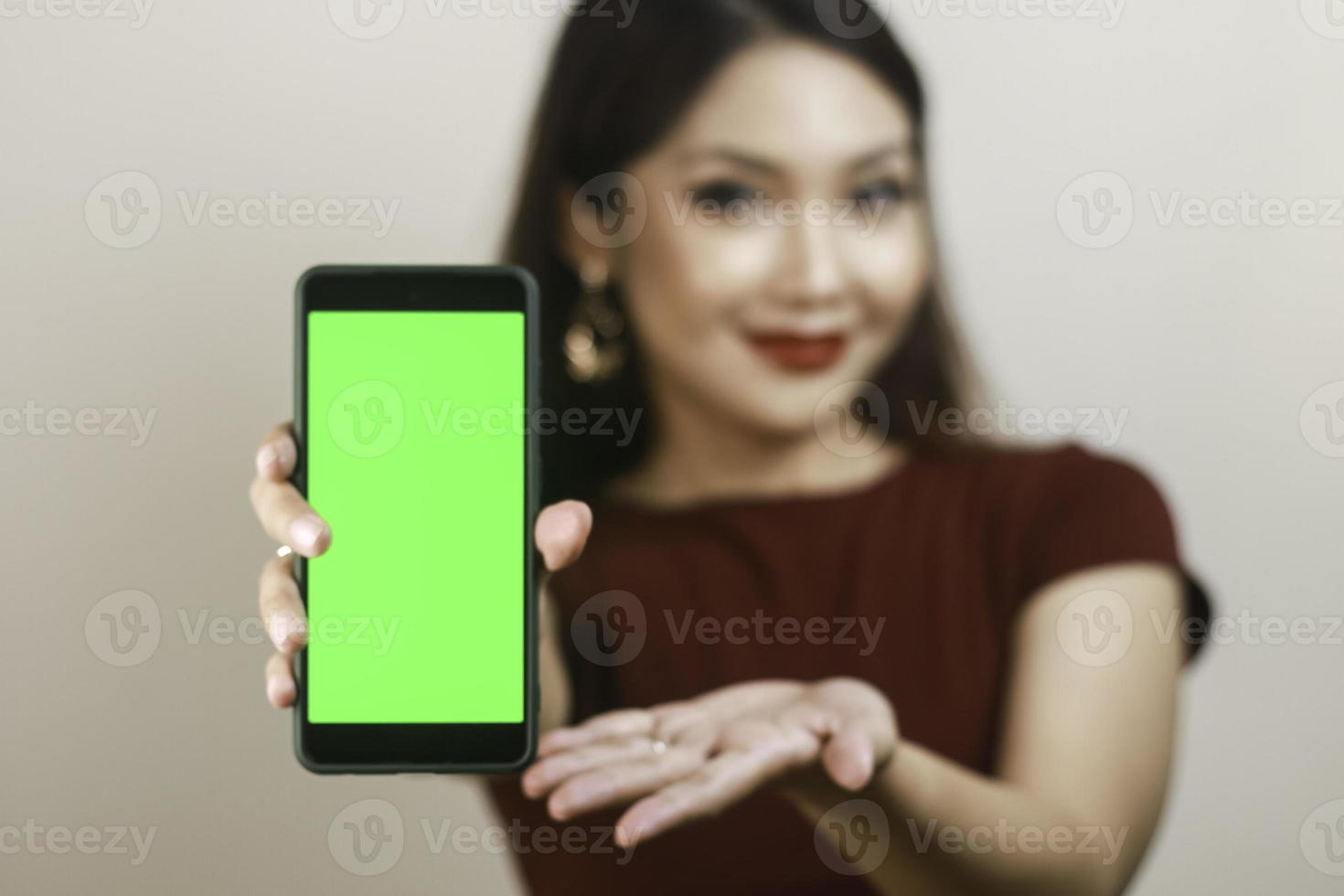 Happy and smiling young Asian woman showing and pointing to a green blank screen. photo