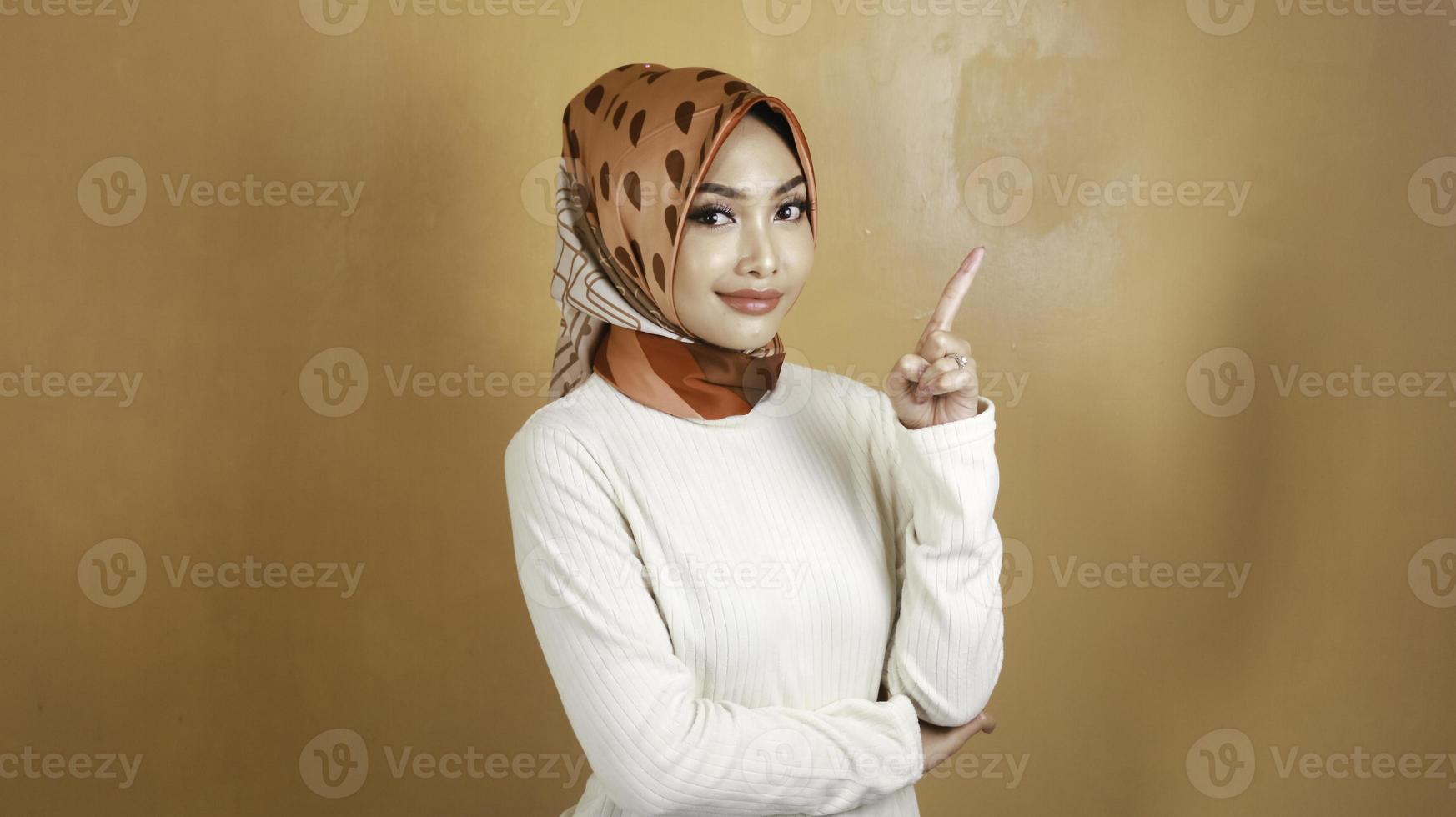 Cheerful young Muslim Asian woman pointing above to copy space with smile photo