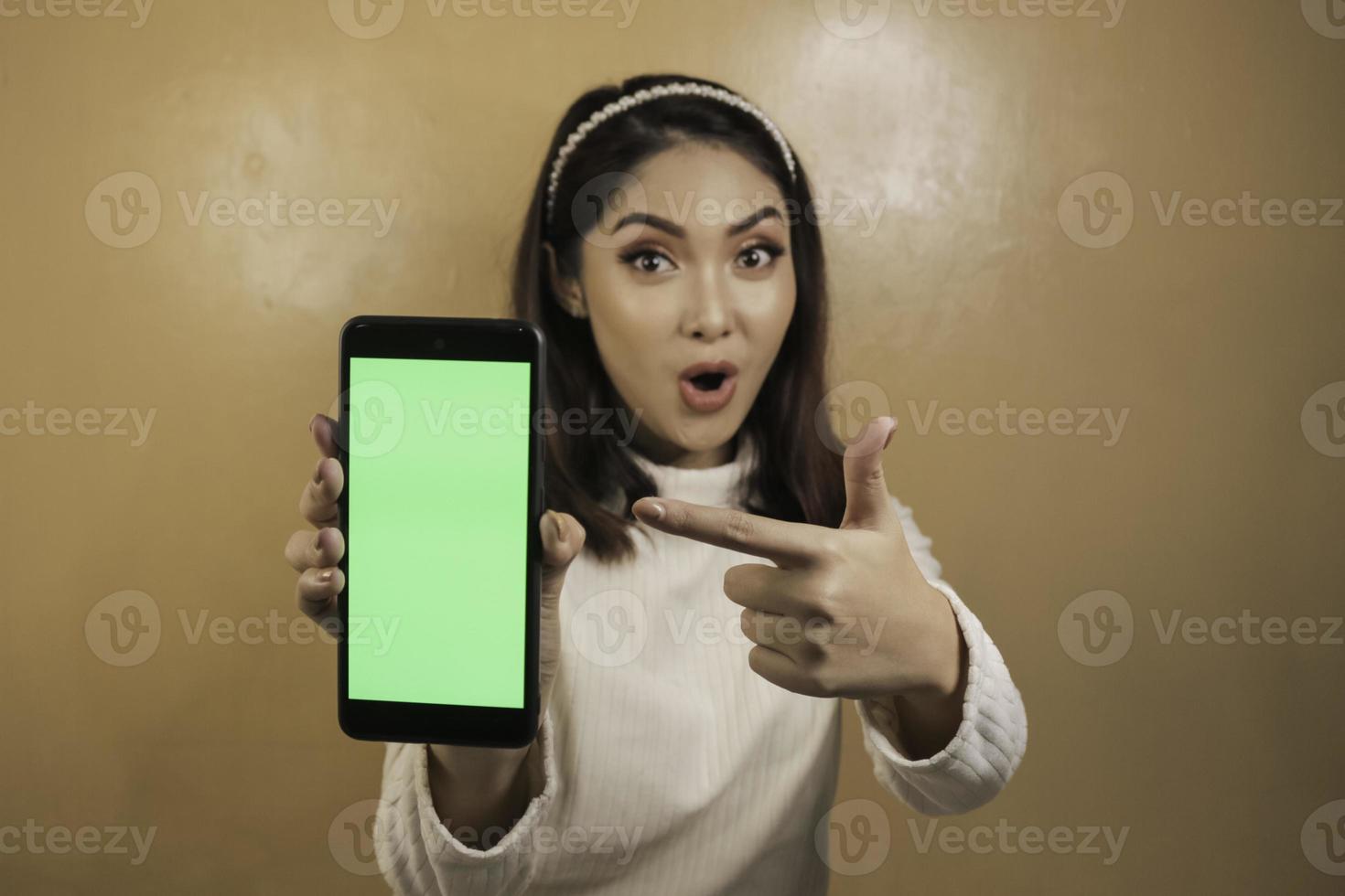 Asian beautiful girl is shocked show green screen in smartphone with white shirt photo