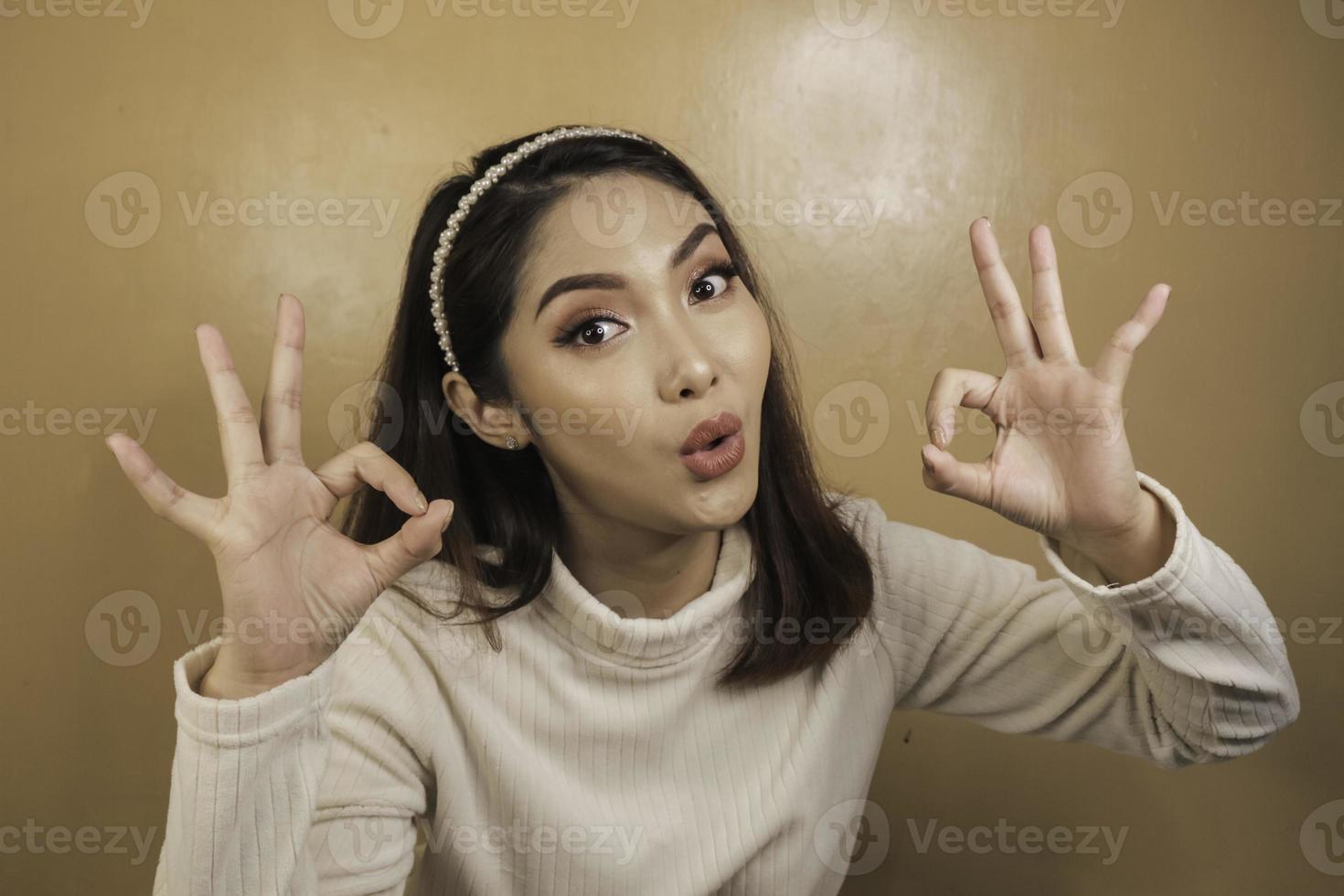 Shock face of a young Asian woman with OK sign wearing a white shirt. Advertisement concept. photo