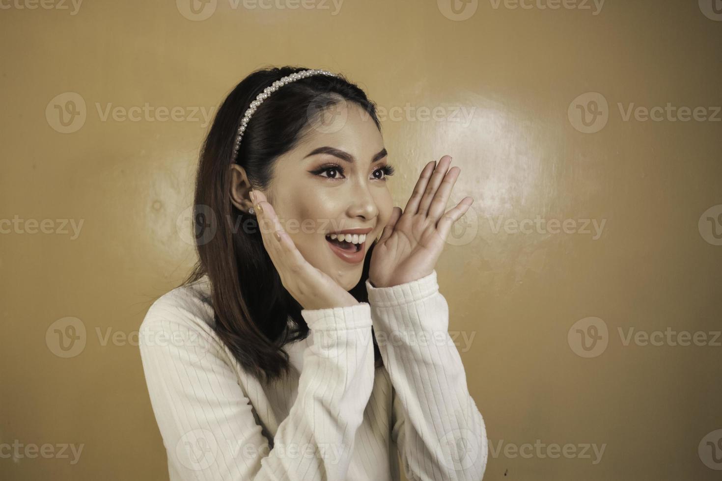 Atractiva mujer asiática joven con cara de asombro apoyando la barbilla en la mano foto