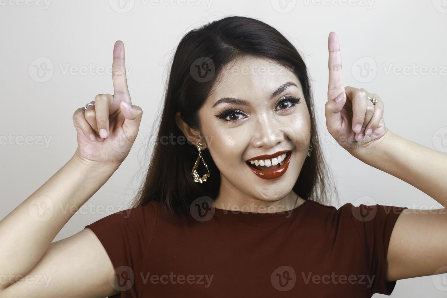 Shock face of a young Asian woman wearing a red shirt pointing upwards. Advertisement concept. photo