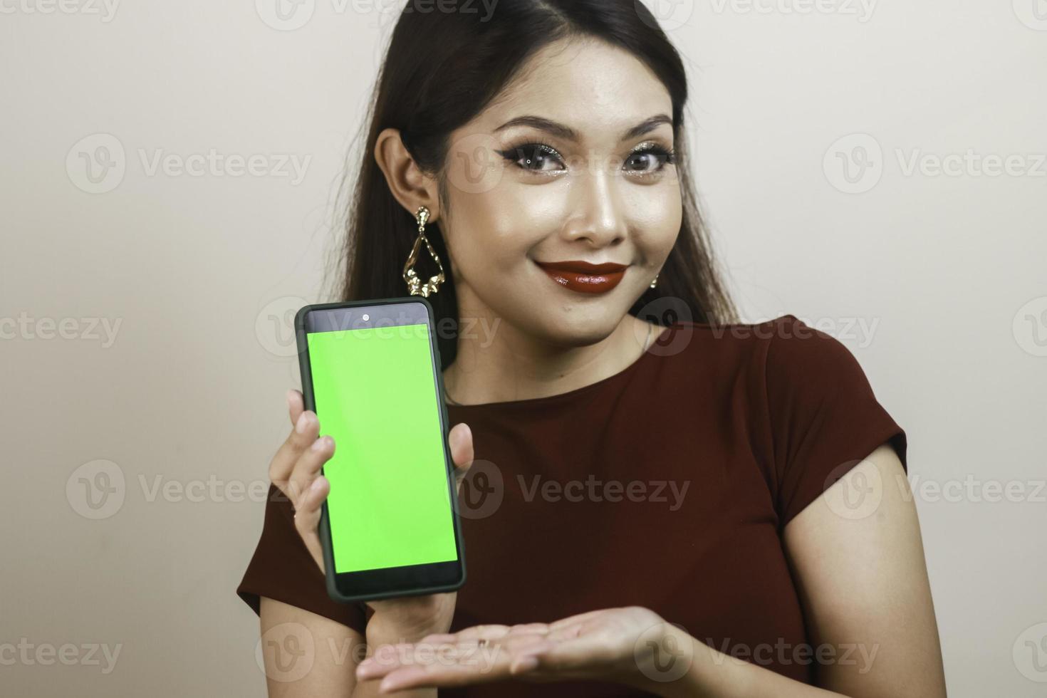 Happy and smiling young Asian woman showing and pointing to a green blank screen. photo