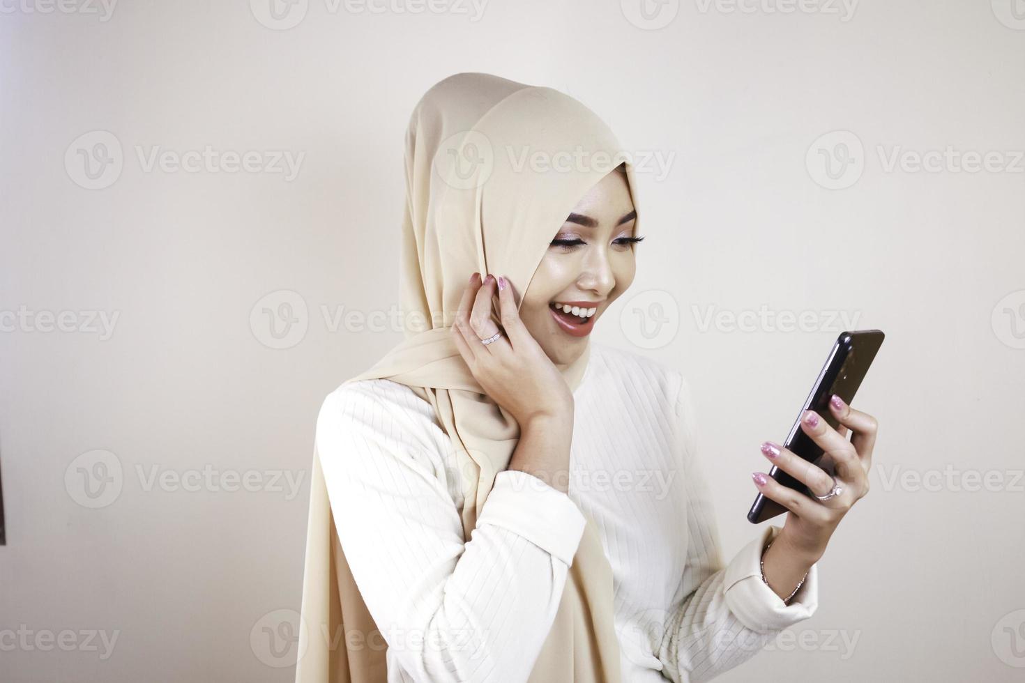 Portrait of cheerful young Muslim Asian woman smiling while looking at her cellphone photo