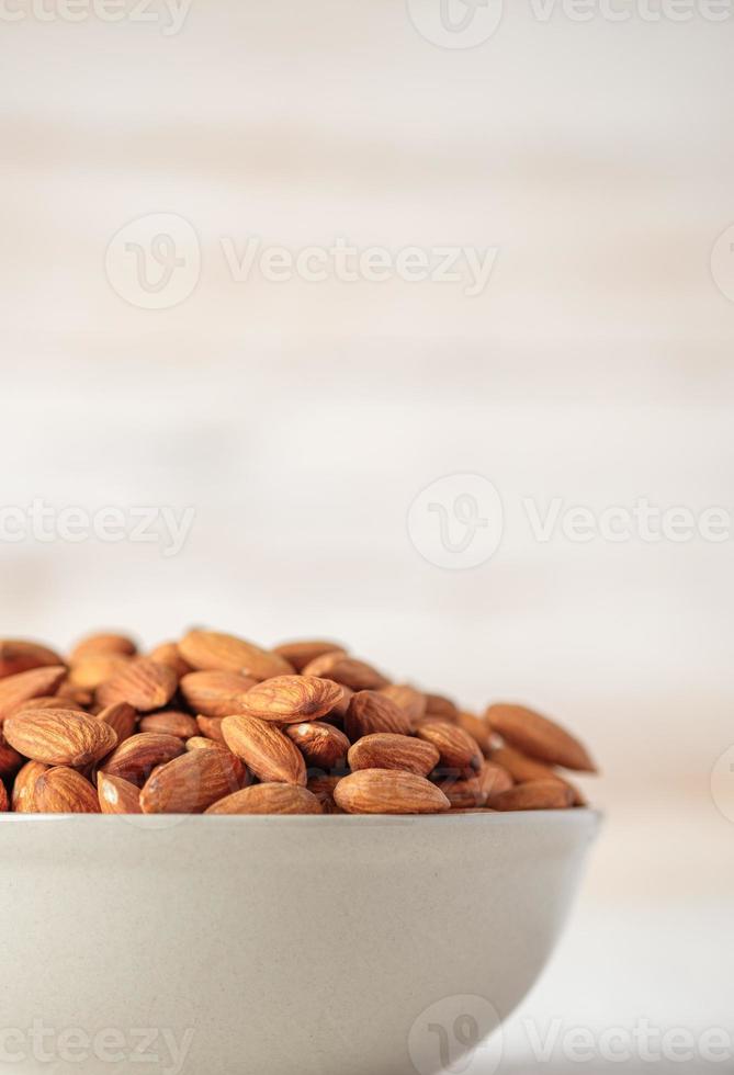 almendras en cuenco de cerámica sobre mesa de madera blanca. materia prima dietética orgánica foto