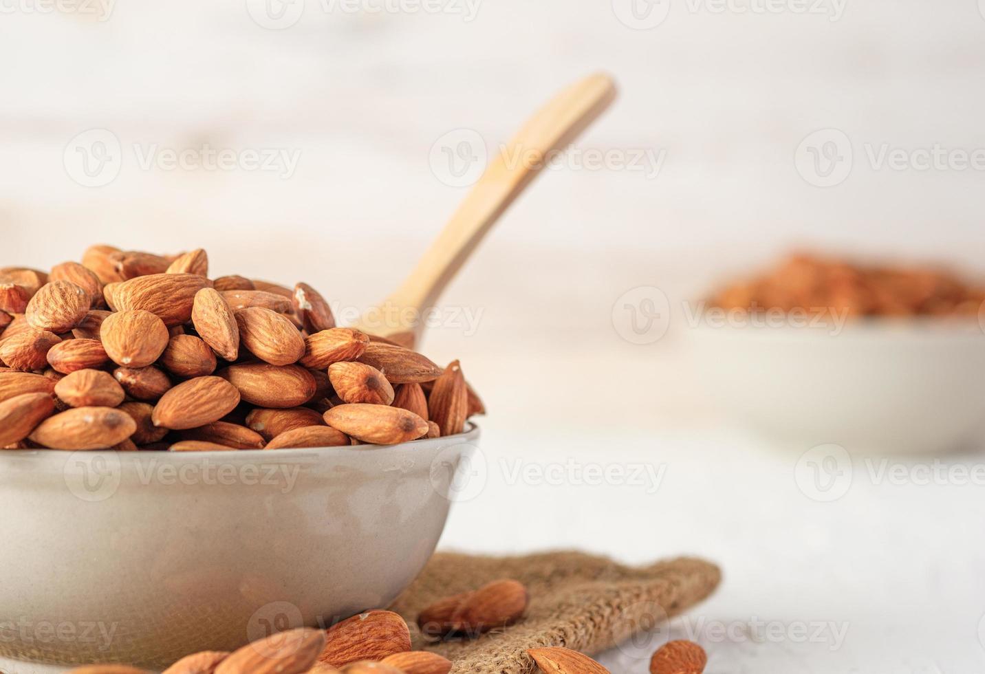 almendras en cuenco de cerámica sobre mesa de madera blanca. materia prima dietética orgánica foto